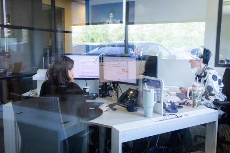 Deux collaboratrices travaillant à leurs bureaux, mur jaune en fond